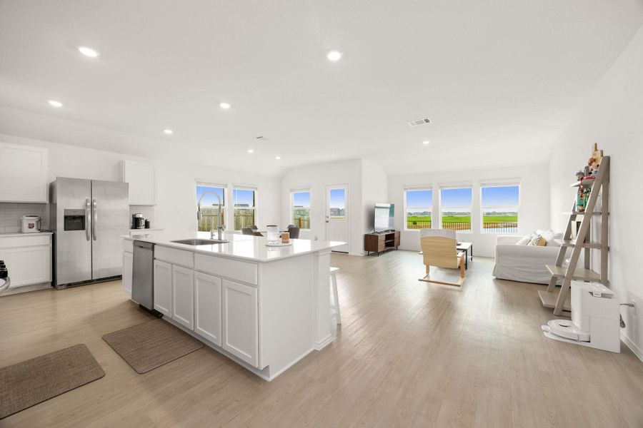 An open-concept living space with a pristine kitchen island transitions seamlessly into a well-lit living area, featuring numerous windows and ample natural illumination.