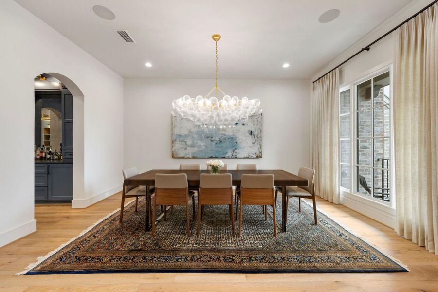 Elegant formal dining room featuring wide-plank wood flooring, a striking designer chandelier, and large windows that fill the space with natural light, complemented by built-in surround sound speakers—perfect for hosting memorable gatherings.
