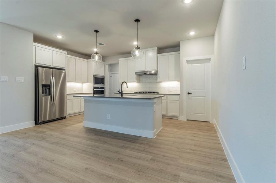 Kitchen with dark countertops, stainless steel appliances, white cabinetry, pendant lighting, and an island with sink