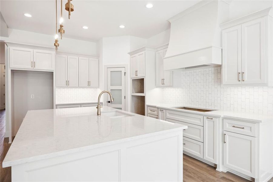 Kitchen with cooktop, premium range hood, an island with sink, pendant lighting, and white cabinets