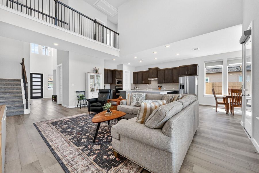 Living room with light wood-style LVP flooring, a high ceiling, and recessed lighting. Open above to the second story.