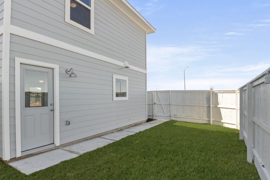 Image of a cottage home backyard with a backdoor, a white fence, cement walkway, and a blue sky Image of a cottage home backyard with a backdoor, a white fence, cement walkway, and a blue sky