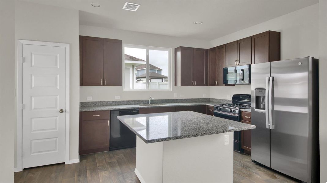 Kitchen with stainless steel appliances, dark wood finish cabinets, light stone counters, a center island, and dark wood finished floors