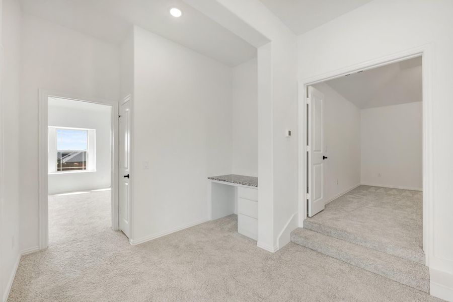 Carpeted hallway with built-in desk nook, white walls, and doors leading to adjacent rooms