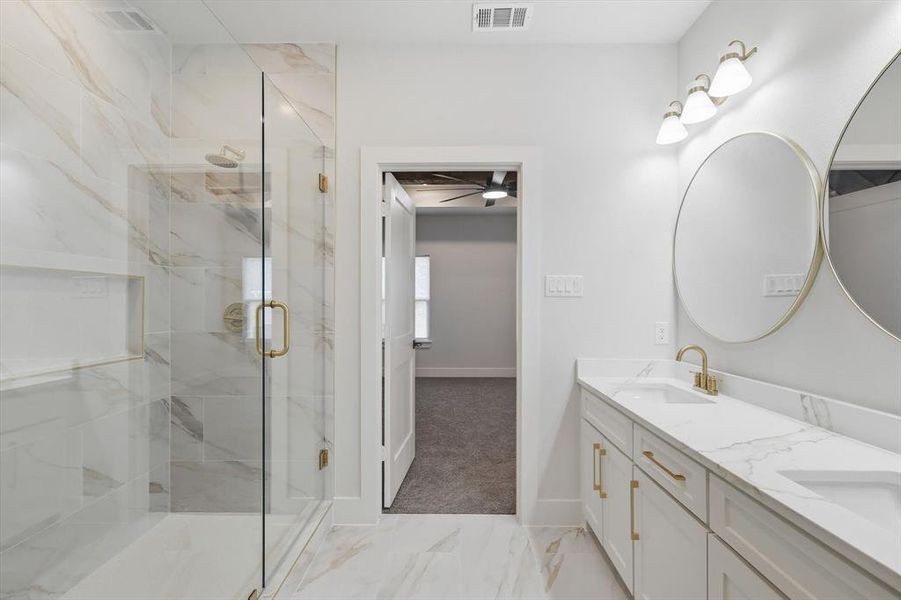 Full bath with a marble finish shower, double vanity, light marble finish floors, and ceiling fan