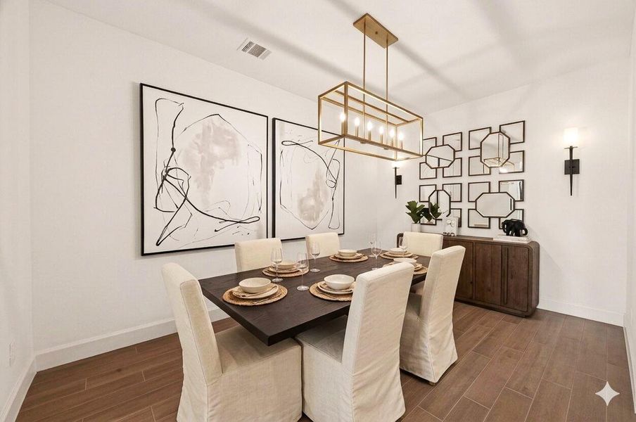 This elegant dining room features a modern table set for six, with comfortable white slip-covered chairs. The room is accented by abstract wall art, a geometric mirror arrangement, and a stylish chandelier, creating a sophisticated and inviting atmosphere. Photos have been virtually staged to help illustrate the potential of the space.
