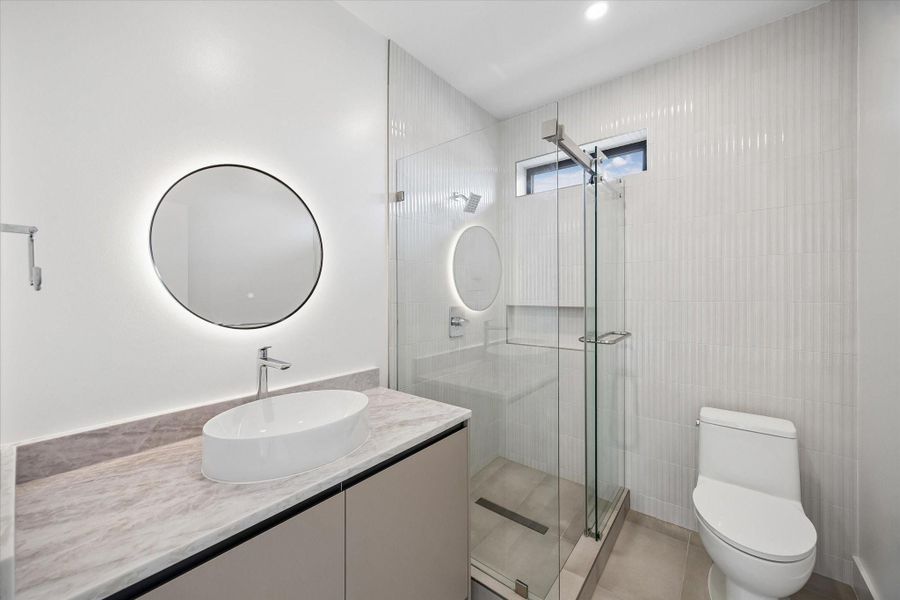 Modern bathroom featuring a stylish circular mirror with backlighting, a spacious glass-enclosed shower, and elegant fixtures. Modern bathroom featuring a stylish circular mirror with backlighting, a spacious glass-enclosed shower, and elegant fixtures.