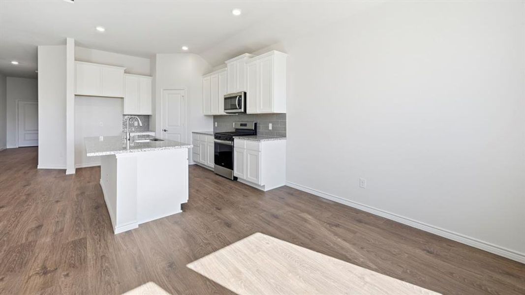 Modern kitchen featuring white cabinetry, stainless steel appliances, a center island with sink, and wood-finish flooring Modern kitchen featuring white cabinetry, stainless steel appliances, a center island with sink, and wood-finish flooring