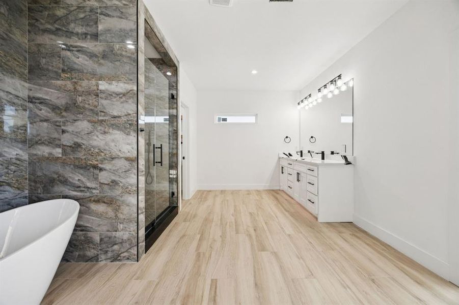 Bathroom featuring a freestanding tub, double vanity, light wood finished floors, a marble finish shower, and recessed lighting
