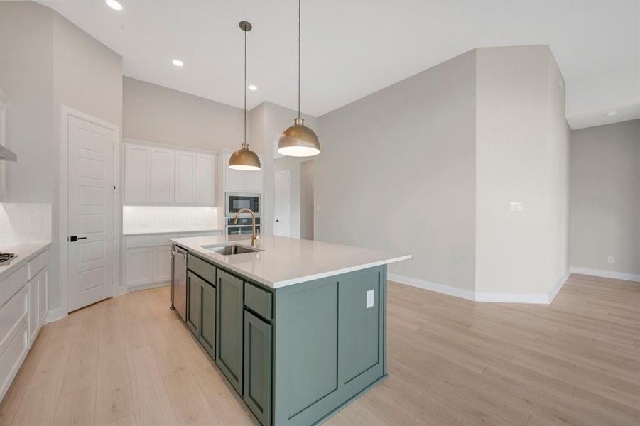 Kitchen featuring a central island with a sink and gold-finish faucet, white countertops, built-in stainless steel appliances, and light wood-finish flooring