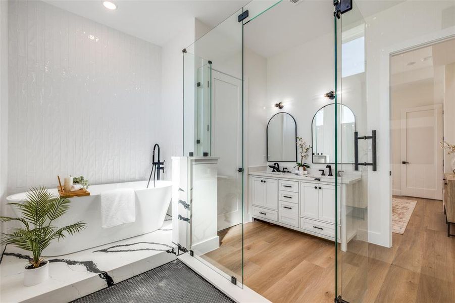 Full bath with light wood-style flooring, double vanity, a freestanding tub, and recessed lighting