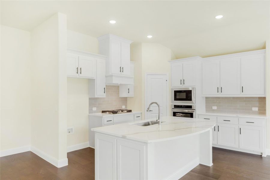 Kitchen with white cabinets, center island with sink, stainless appliances, tile backsplash, and dark hardwood floors Kitchen with white cabinets, center island with sink, stainless appliances, tile backsplash, and dark hardwood floors