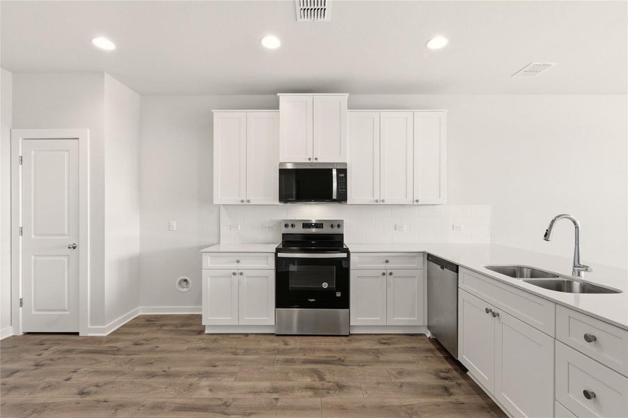Kitchen with decorative backsplash, appliances with stainless steel finishes, white cabinetry, recessed lighting, and light stone counters