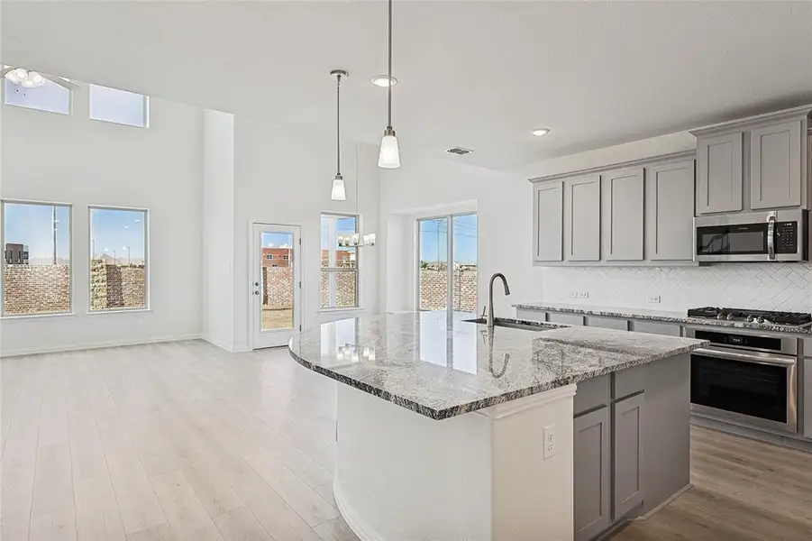 Kitchen featuring gray cabinetry, tasteful backsplash, light stone counters, stainless steel appliances, and a high ceiling Kitchen featuring gray cabinetry, tasteful backsplash, light stone counters, stainless steel appliances, and a high ceiling