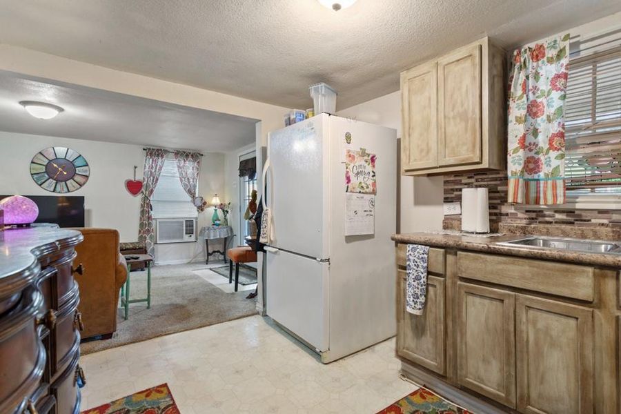 Kitchen featuring freestanding refrigerator, open floor plan, decorative backsplash, light flooring, and a textured ceiling