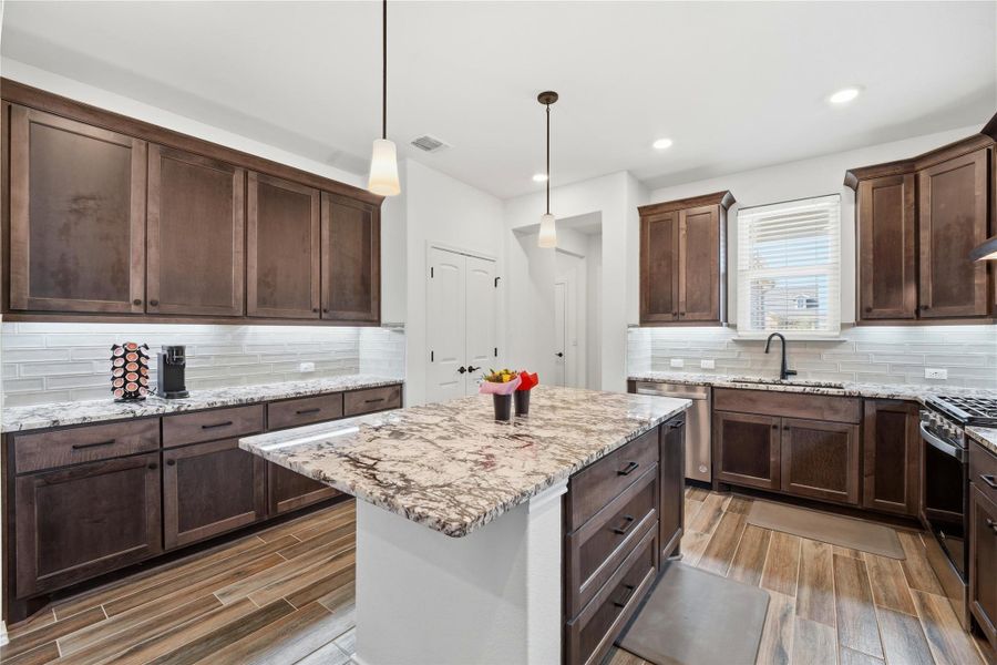 Kitchen featuring light stone countertops, a kitchen island, hanging light fixtures, dark wood finish cabinetry, and wood finish floors