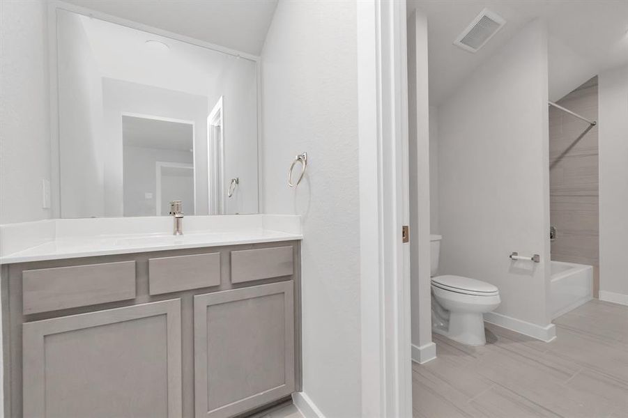 Experience convenience in the secondary bathroom, designed for Jack and Jill arrangements, now with a separate vanity area. This well-appointed space showcases stylish tile flooring, a bath/shower combo with an elegant tile surround, and light-stained wood cabinets. The beautiful light countertop adds a touch of sophistication, combining functionality and aesthetics seamlessly. Sample photo of completed home with similar floor plan. As-built interior colors and selections may vary.