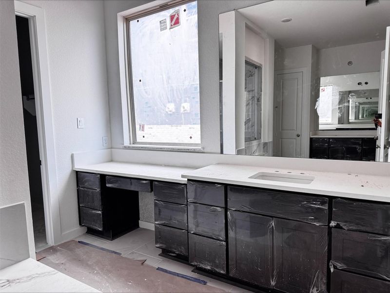 This elegant primary bath features an expansive vanity with abundant storage, a large statement mirror, and a bright, spacious layout.