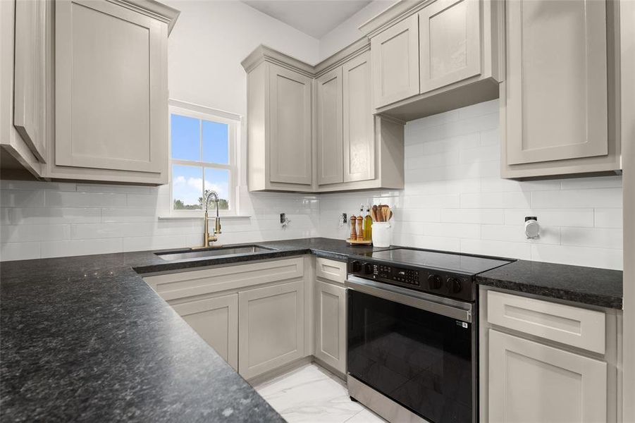 Kitchen featuring light-toned cabinetry, dark countertops, a stainless steel range, and a brass-finished faucet Kitchen featuring light-toned cabinetry, dark countertops, a stainless steel range, and a brass-finished faucet