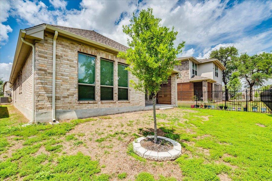 This property features a brick exterior with vertical windows, an expansive yard with a lawn, and a young tree with a decorative stone border