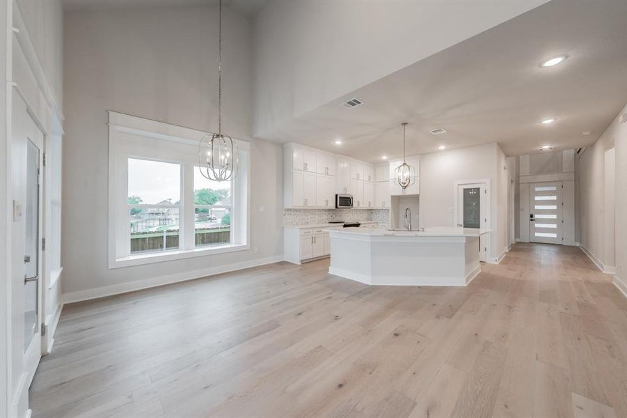 Kitchen featuring a chandelier, white cabinets, open floor plan, a kitchen island with sink, and light wood-type flooring