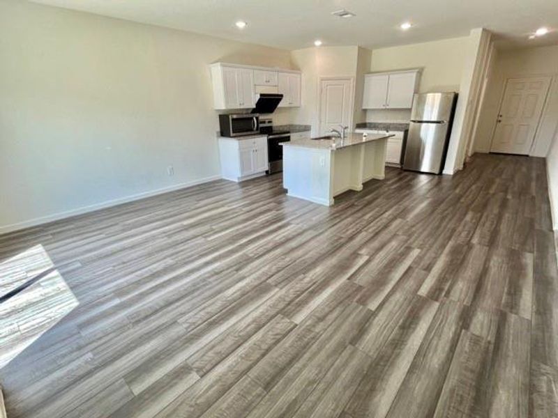 Kitchen featuring white cabinetry, wood-type flooring, light stone counters, a center island with sink, and appliances with stainless steel finishes