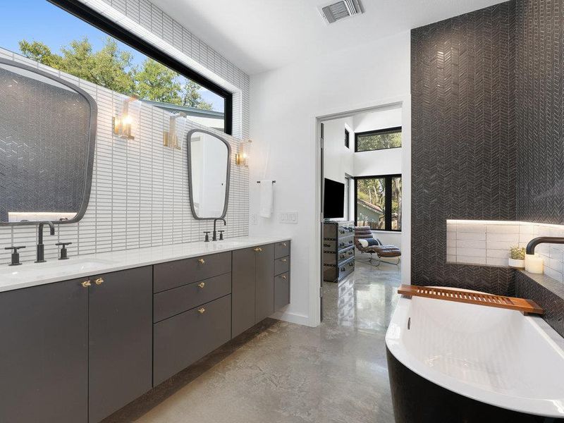 Ensuite bathroom with a freestanding bath, double vanity, finished concrete flooring, and backsplash