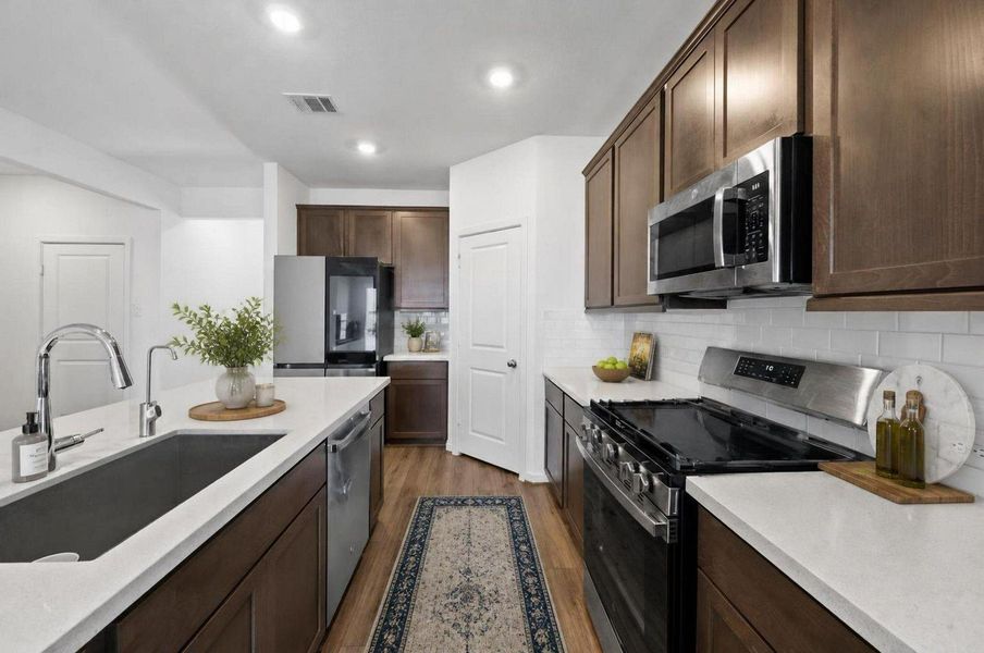 This kitchen angle highlights the gas range, microwave, cabinetry, and functional prep layout. The warm cabinet finish adds contrast against the light walls and counters. Virtually staged. This kitchen angle highlights the gas range, microwave, cabinetry, and functional prep layout. The warm cabinet finish adds contrast against the light walls and counters. Virtually staged.
