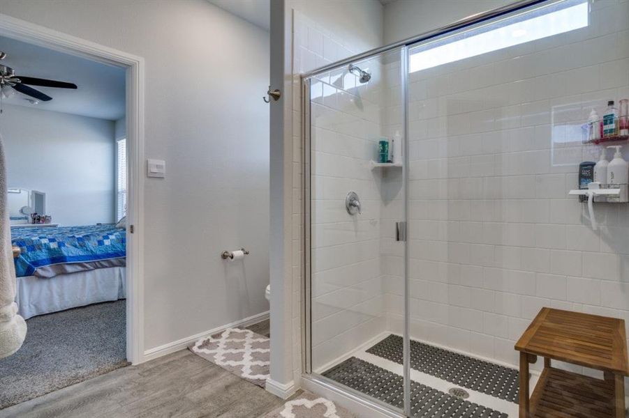 Bathroom featuring wood finished floors, baseboards, ensuite bath, a stall shower, and toilet