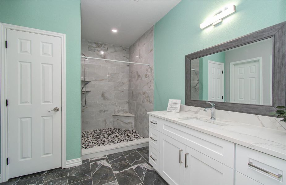 Modern bathroom featuring a spacious walk-in shower with a pebble stone floor, elegant gray tile walls, and a sleek white vanity with a large framed mirror. The light teal wall adds a refreshing touch.