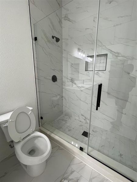 Full bathroom with marble look tile flooring, a marble finish shower, and a textured wall
