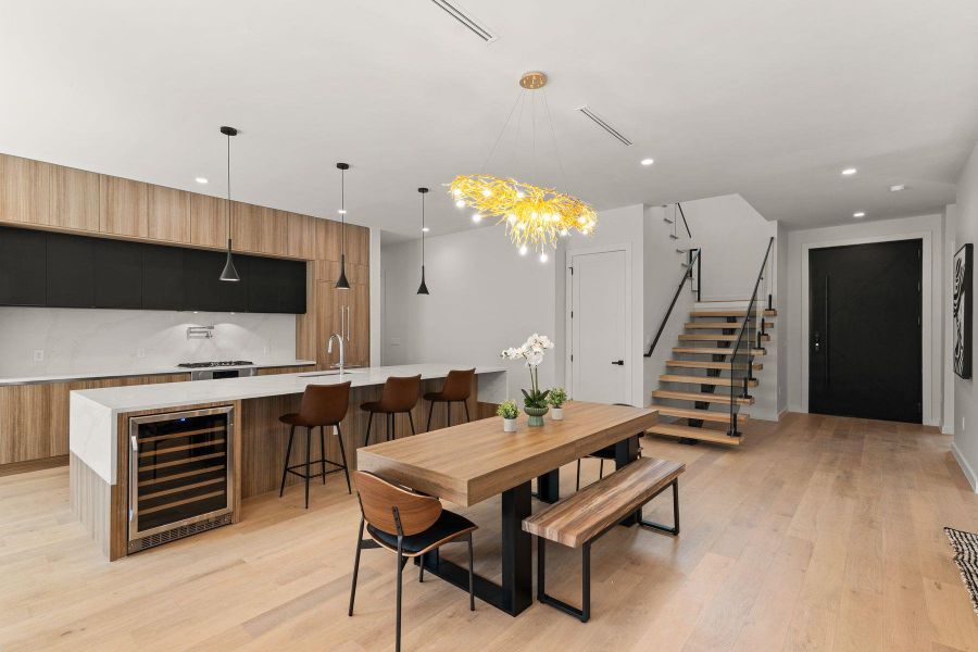 An open floorplan showcases a modern kitchen, dining space, and floating stairs over hardwood flooring.