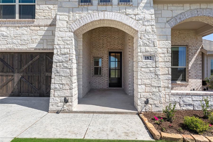 Home entrance with stone and brick arched entryway, black front door, and wood garage door beside it.