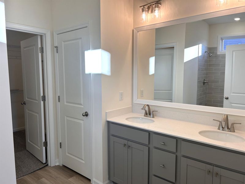 Bathroom featuring double vanity, tiled shower, light wood-style flooring, and a walk in closet