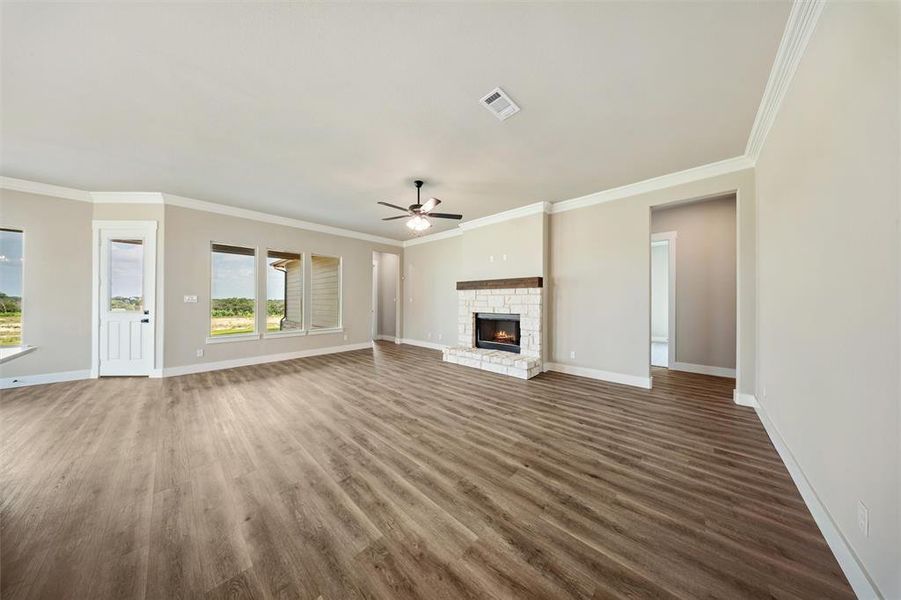 Unfurnished living room with a ceiling fan, dark wood-style floors, a fireplace, and ornamental molding Unfurnished living room with a ceiling fan, dark wood-style floors, a fireplace, and ornamental molding