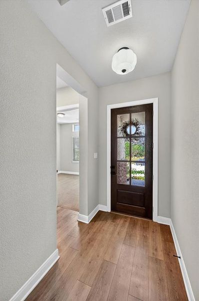 Entryway featuring wood-finish flooring, a dark wood-paneled door with glass inserts, and a flush-mount ceiling light Entryway featuring wood-finish flooring, a dark wood-paneled door with glass inserts, and a flush-mount ceiling light