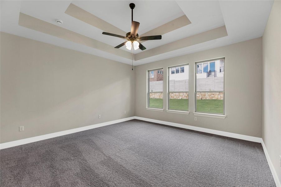 Empty room with a tray ceiling, carpet flooring, and ceiling fan