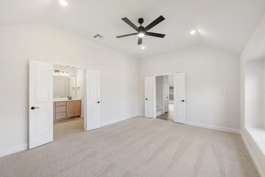 Spacious bedroom with carpet, ceiling fan, and open doors leading to ensuite bathroom and hallway
