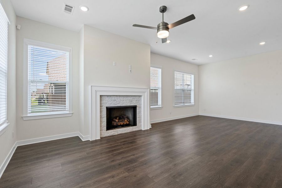 Living space featuring a fireplace with a textured stone surround and white mantel, wood-finish flooring, recessed lighting, and a ceiling fan Living space featuring a fireplace with a textured stone surround and white mantel, wood-finish flooring, recessed lighting, and a ceiling fan