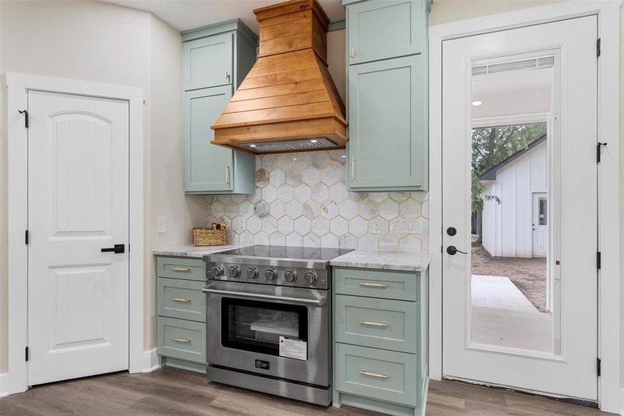 Kitchen featuring stainless steel range, green cabinetry, custom range hood, and dark wood finished floors
