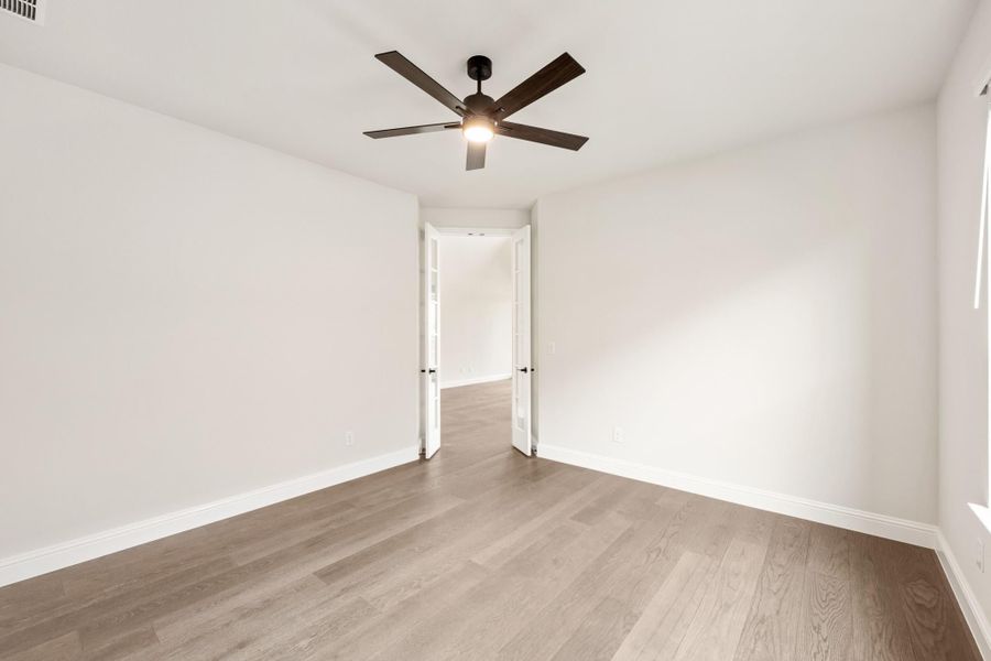 Empty bedroom with light wood floors, white walls, ceiling fan, and open French doors Empty bedroom with light wood floors, white walls, ceiling fan, and open French doors