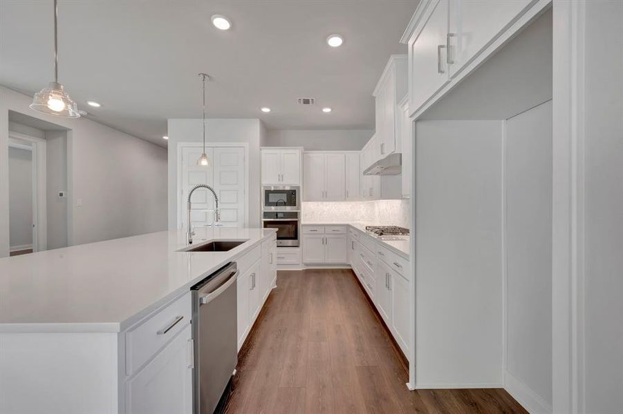Kitchen featuring white cabinets, stainless steel appliances, dark wood finished floors, a center island with sink, and light stone counters