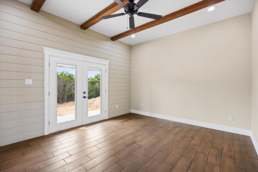 Unfurnished room featuring beamed ceiling, french doors, wooden walls, a ceiling fan, and dark wood-type flooring Unfurnished room featuring beamed ceiling, french doors, wooden walls, a ceiling fan, and dark wood-type flooring