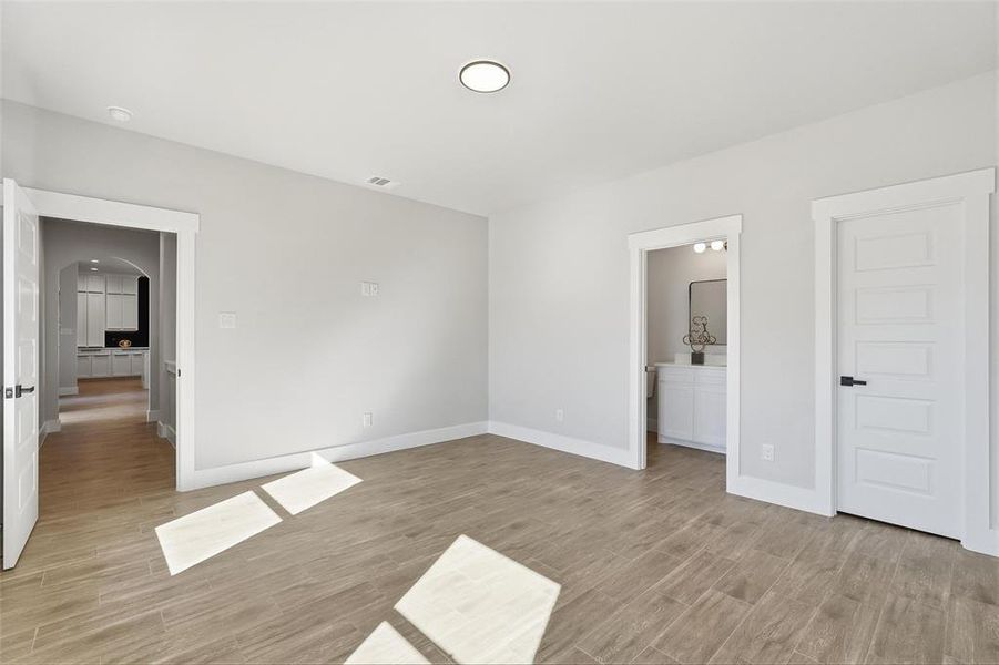 Unfurnished bedroom featuring arched walkways, light wood finished floors, and ensuite bath