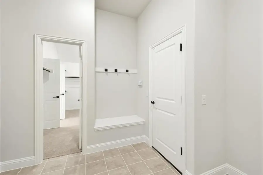 Entry area with neutral-toned tiled flooring, white baseboards, and a built-in bench Entry area with neutral-toned tiled flooring, white baseboards, and a built-in bench
