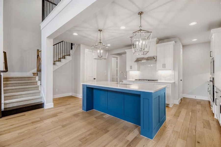 Kitchen with an island with sink, light wood-type flooring, a chandelier, decorative backsplash, and two tone color scheme