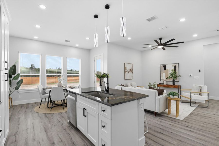 Open-concept living space featuring wood-finish flooring, a kitchen island with stone countertops, recessed lighting, a ceiling fan, and multiple windows