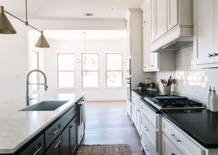 Kitchen with white cabinetry, sink, hanging light fixtures, a center island with sink, and hardwood / wood-style flooring