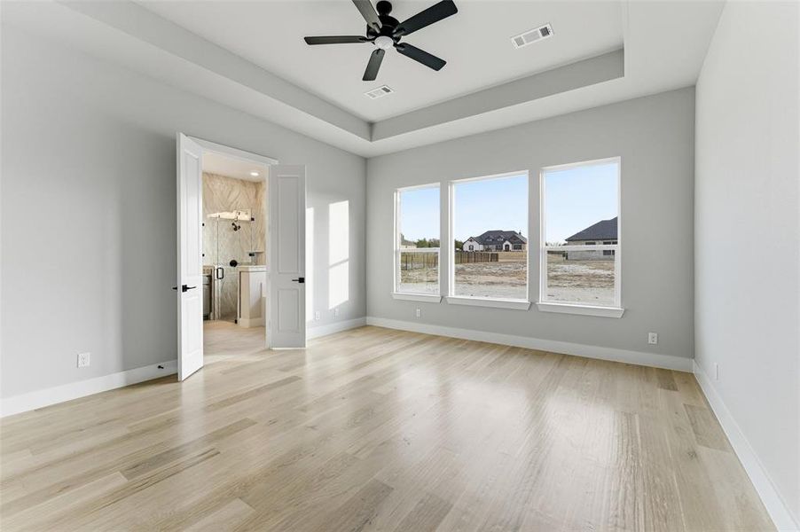 Unfurnished bedroom with a tray ceiling, light wood finished floors, a ceiling fan, and connected bathroom