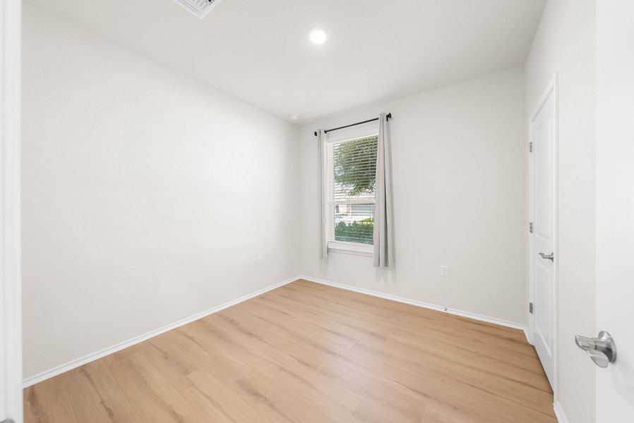 A well-lit bedroom features durable plank flooring and a window offering views of the exterior. A well-lit bedroom features durable plank flooring and a window offering views of the exterior.